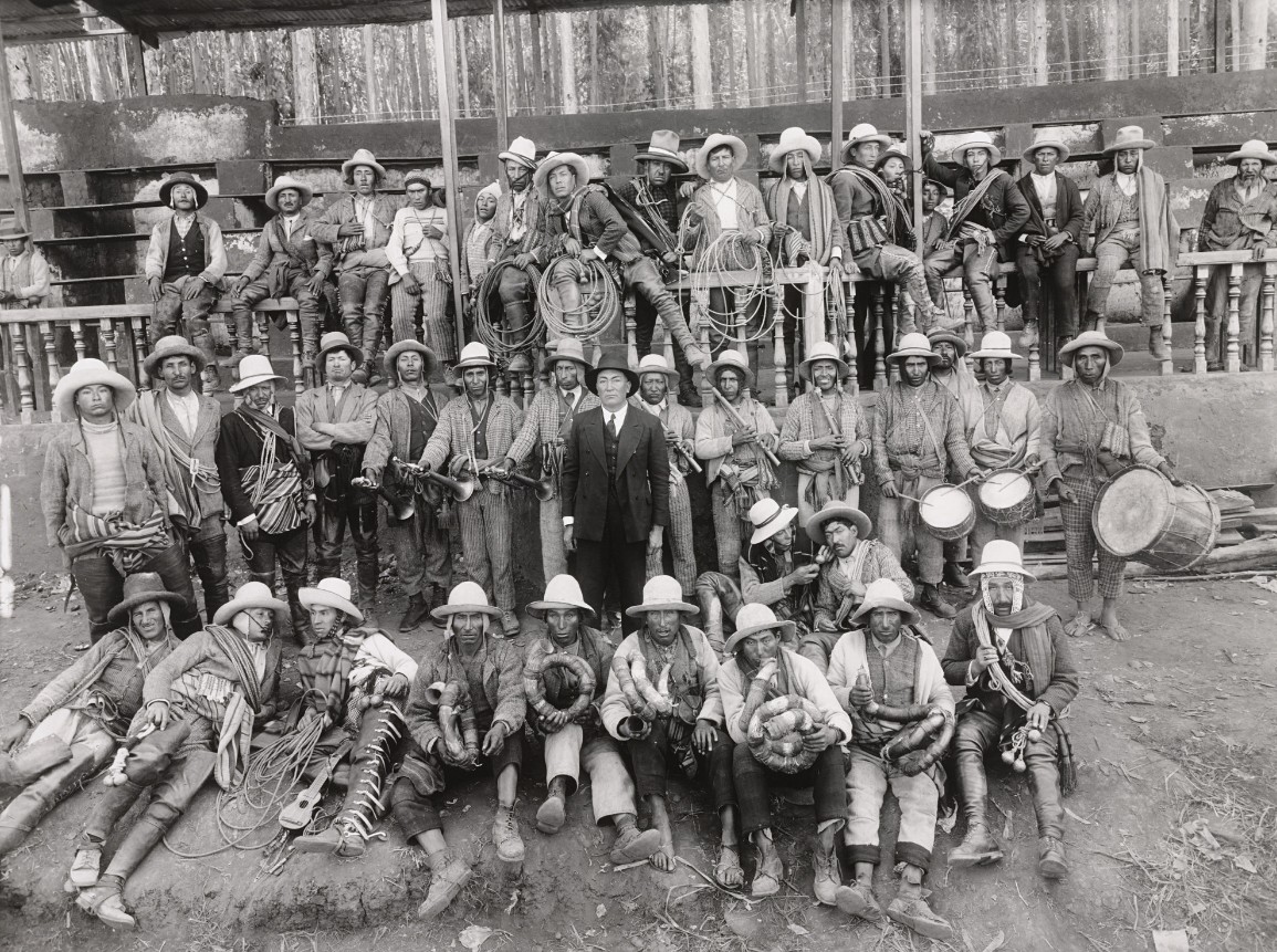 Hacienda owner in a suit at the center, surrounded by workers with ropes, horns and drums, photograph by Martín Chambi